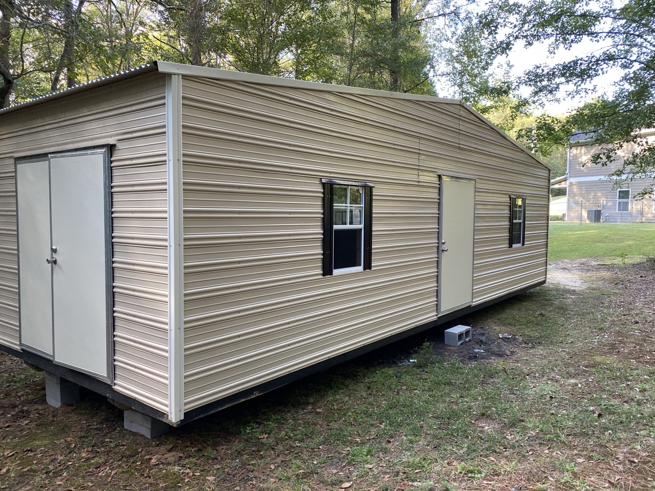 Tan aluminum shed with black shutters, wide view